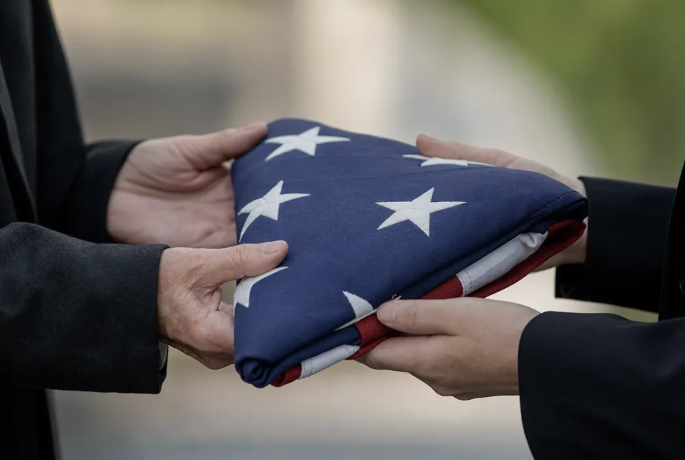 Two people holding a folded American flag, representing a surviving family after the death of a civilian overseas contractor